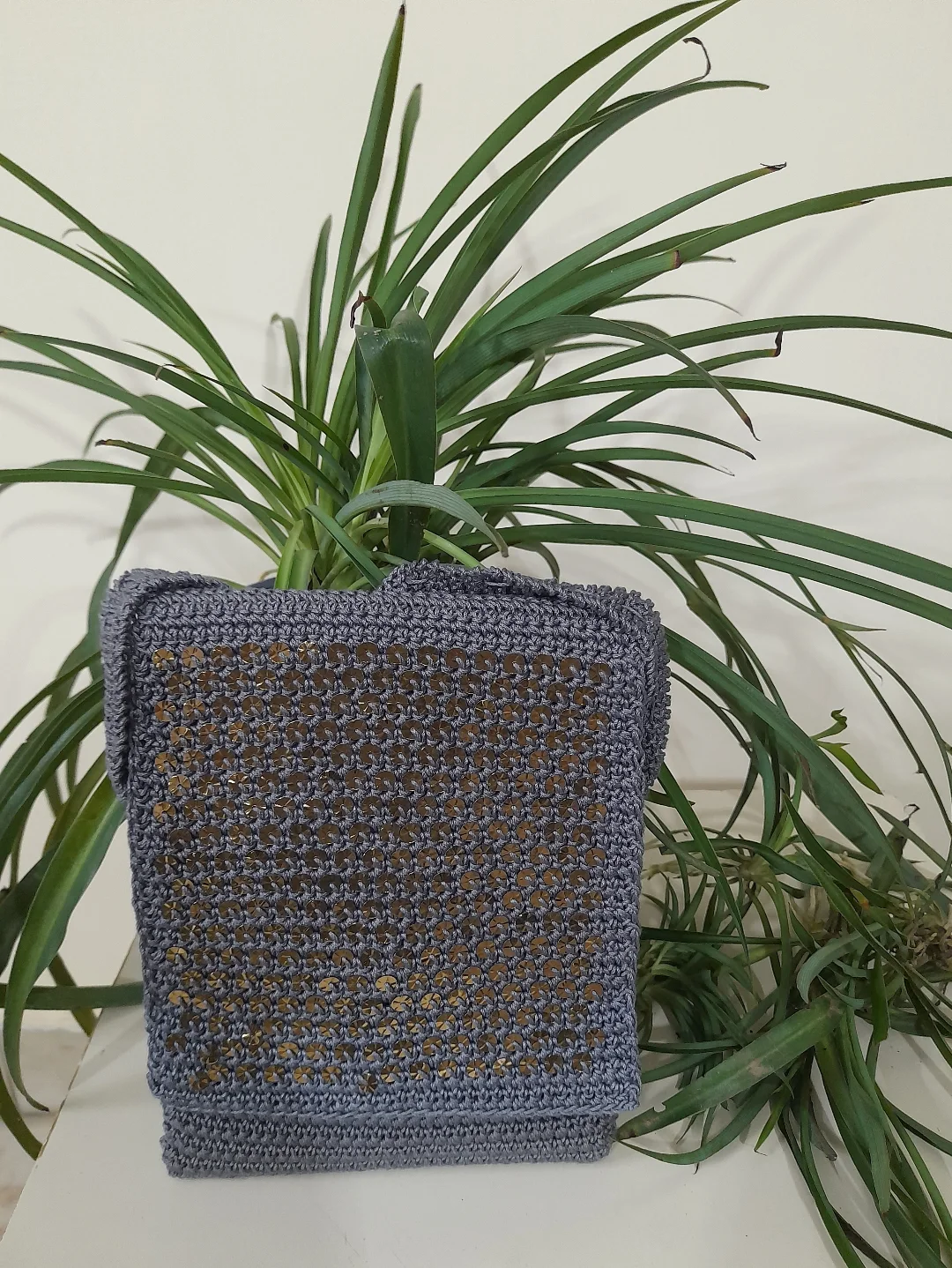 A grey crochet sling bag with a gold chain strap.