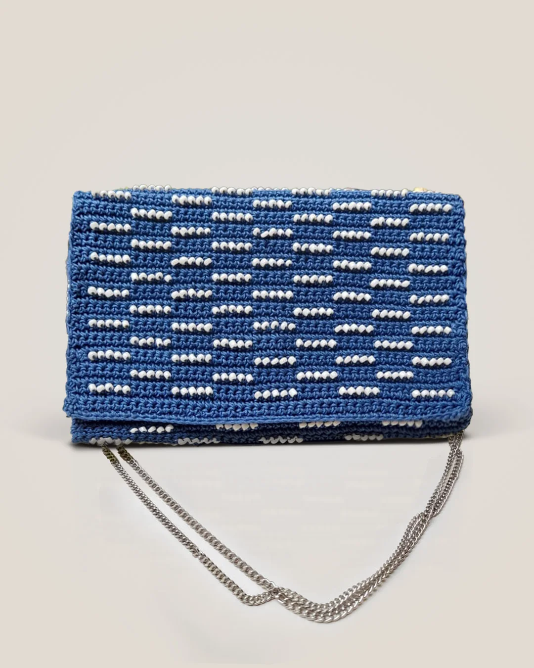 A cobalt-blue crochet clutch with a fold-over flap and short rows of white beads, on a silver chain.
