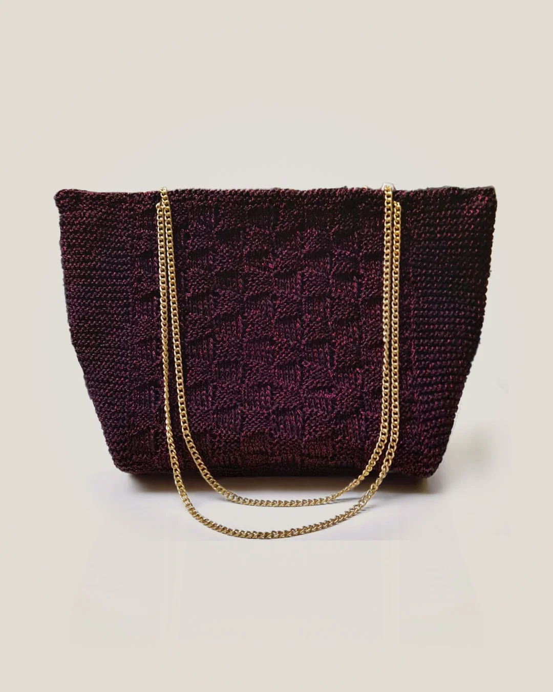 A wine-coloured crochet tote with a raised block texture, a soft sheen and a gold chain strap.