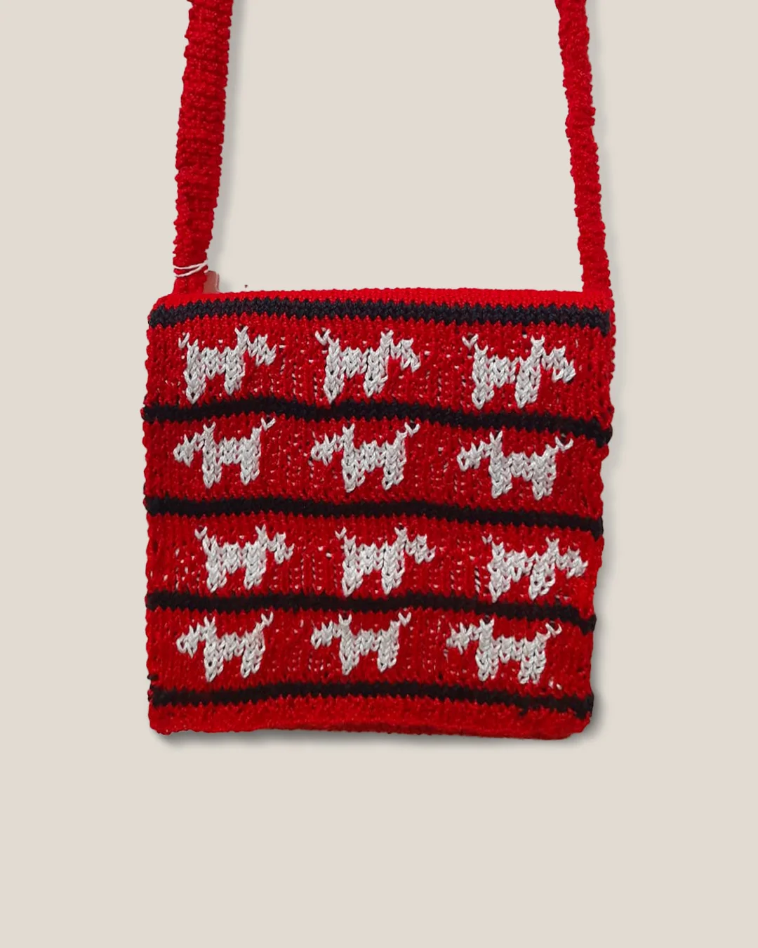 A red crochet sling bag with four rows of small white dogs between black stripes.