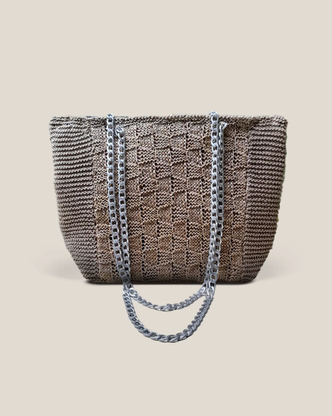 A taupe crochet tote with a raised block panel and a chunky silver chain strap.